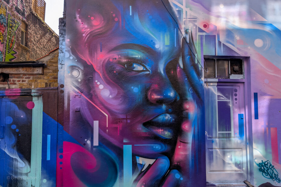 Colourful street art mural with a portrait of a woman painted in purple and blue with abstract shapes and lighting.