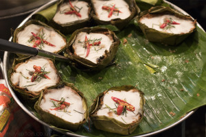 Close up of a tray with several circular dishes made of ricde wrapped in vine leaves, all arranged on a C shape on top of a larger green vine leaf. What to Eat in Chiang Mai Old City