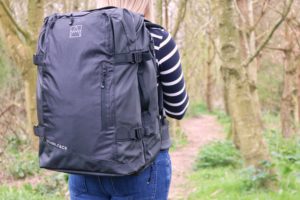 woman walking in forest carrying black travel backpack