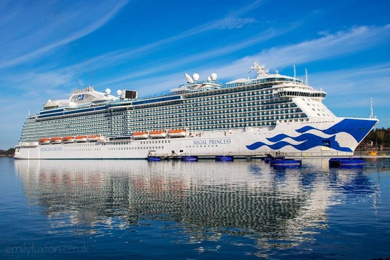 Shot of a white cruise ship on the sea in a harbour against a blue sky with the ship reflected in the water - Regal Princess Review