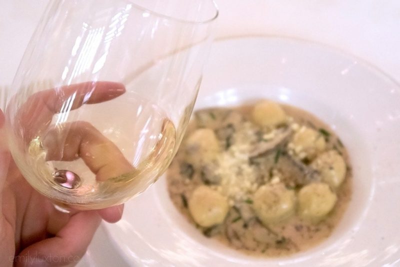 Close up of a hand holding a glass of white wine above a china bowl filled with pasta in a creamy sauce. Wine Makers Dinner Regal Princess food review