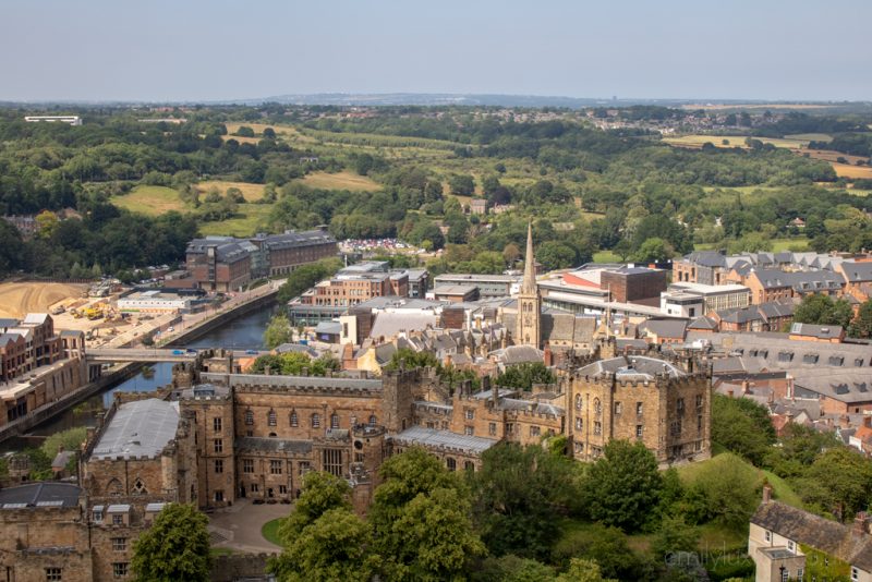 View of Durham city skyline from the top of the Cathedral tower, the city centre is small with the light brown stone castle in front and a church tower rising in the middle, and beyond the city are grassy fields and hills and typical english countryside.  Most beautiful cities in England. 
