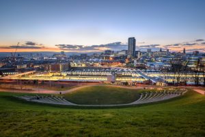 City sklyline of Sheffield England in the evening with clear blue sky and the glow of sunset on the horizon behind skyscrapers lit up for nighttime.