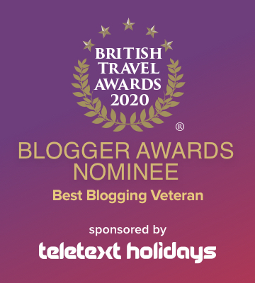 square graphic with a purple and pink background and the British travel Awards 2020 logo surrounded by a gold pattern of leaves and stars. The text over the graphic reads: Blogger Awards Nominee Best Blogging Veteran sponsored by teletext holidays" 