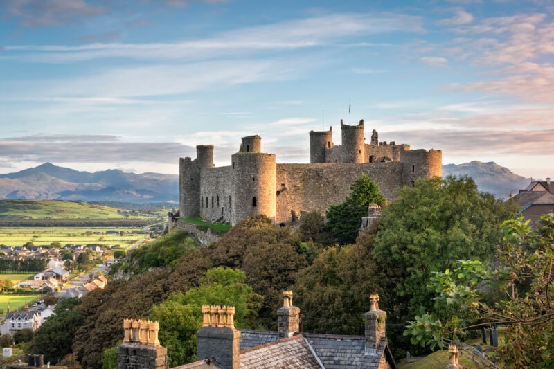 The historic Harlech castle on a hill with multiple towers and battlements overlooking a small town with mountains in the distance. 