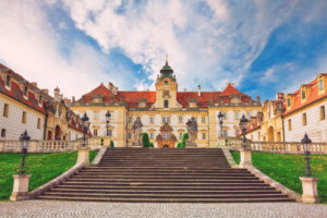 Old historic castle in Valtice, South Moravia. Yellow stone exterior with orange roof. there are stone steps leading up to the castle. sunny day with blue sky.