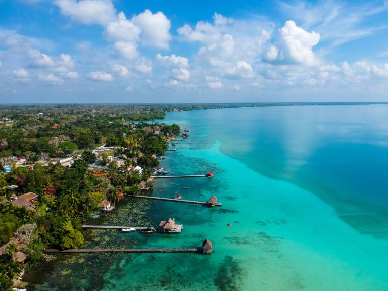 aerial photo of a huge lagoon with striking turquoise water and the shore covered in green tropical forest with several long wooden jetties reaching out into the lake