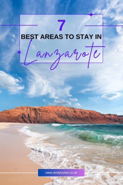 A picturesque beach scene with clear blue skies, turquoise waves, and a sandy shore. In the background, there is a rugged, reddish-brown cliff. Overlaid text reads "7 Best Areas to Stay in Lanzarote" in bold and cursive fonts.