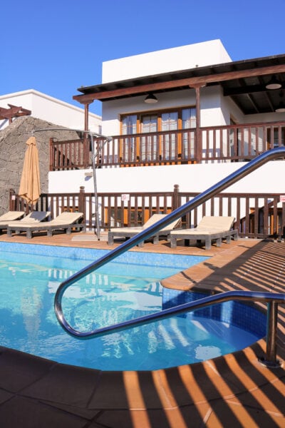 pequena piscina exterior em frente a uma villa de dois andares pintada de branco com acabamentos em madeira num dia ensolarado com céu azul.  Villa em Playa Blanca Lanzarote durante o inverno