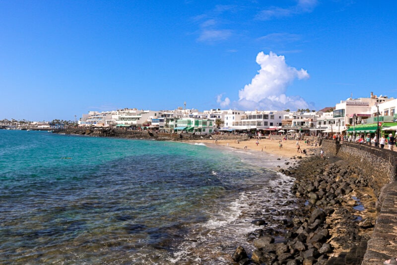 view of a sandy beach in a rocky cove with a small town behind at playa blanca in lanzarote