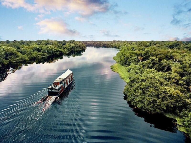 aerial shot of a small cruise ship on the amazon river with rainforest on either side