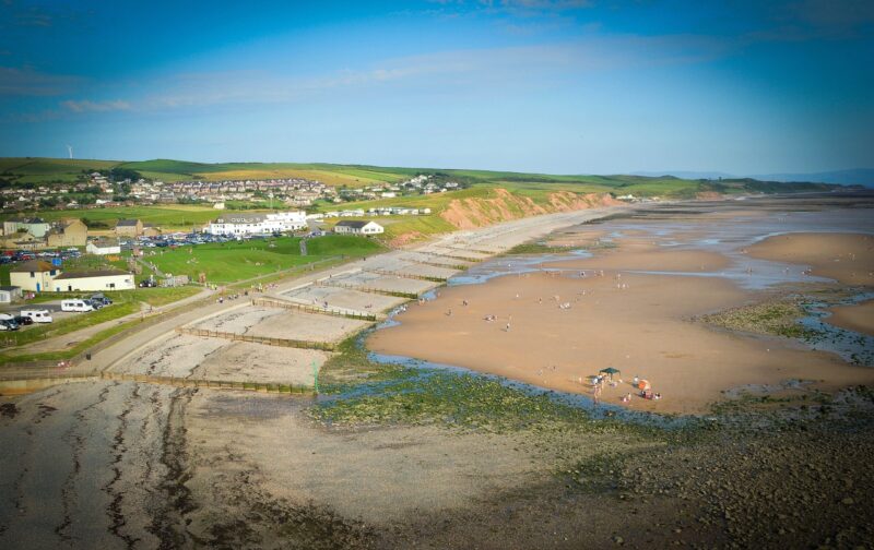 aerial view of St Bees with a large sandy beach at low tide and a small town surroudned by green countryside