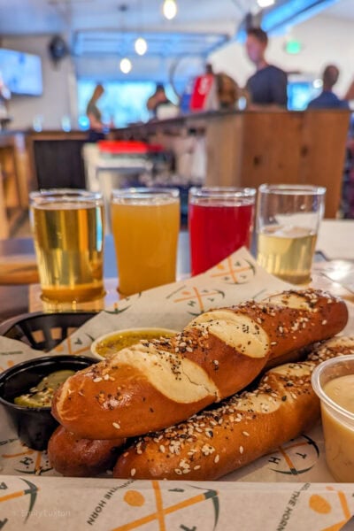 close up of two sticks of bread with a flight of mini beers behind and a bar out of focus behind that