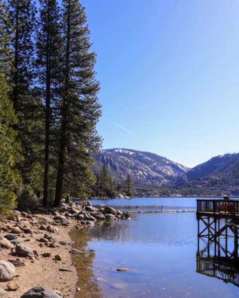 wooden jetty on a large flat lake with mountains and pine forest on the far side reflected in the lake under a clear blue sky - Pinecrest Lake in Tuolumne County California