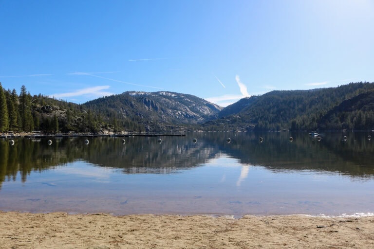 large flat lake with mountains and pine forest on the far side reflected in the lake under a clear blue sky - Pinecrest Lake in Tuolumne County California