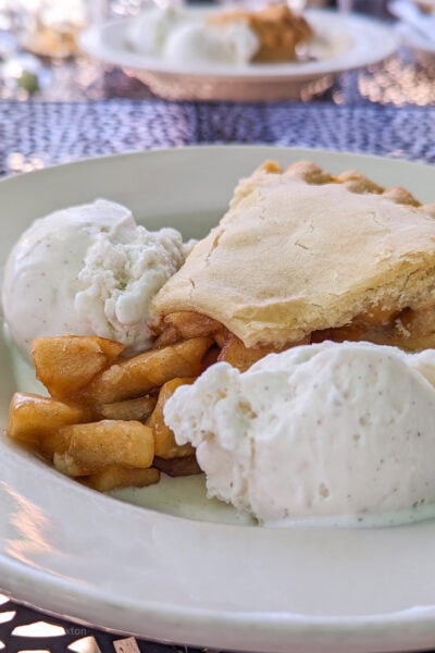 slice of apple pie with the apple chunks spilling out between two scoops of white ice cream in a white china bowl 