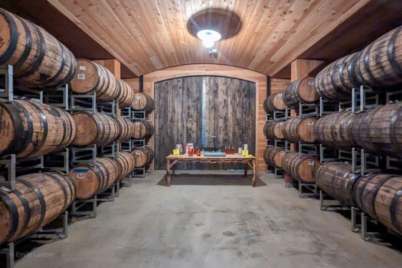 cellar with 3 rows of wooden cider barrels on either side beneath an arched wooden roof.