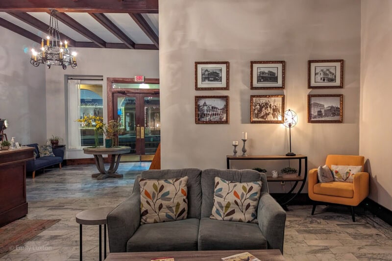 interior of the Sonora Inn lounge with whitewashed walls and dark wooden beams on the cieling. there is a grey sofa in the centre of the room and six framed photographs in a grid on the wall