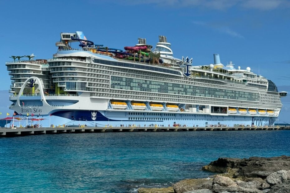 very large white and blue cruise ship at sea with turquoise water and rocks in foreground and blue sky above