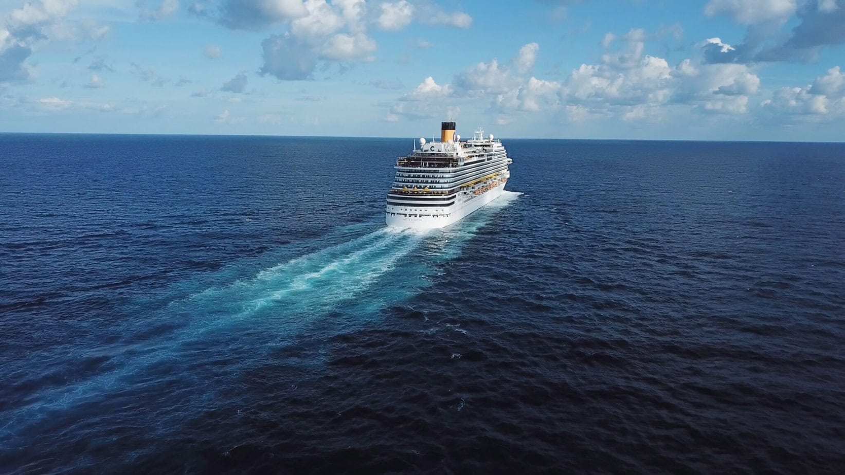 Back of the cruise ship and its beautiful wake on the blue sea surface, seascape. Stock. Aerial view of a beautiful white cruise liner in a sunny day on blue cloudy sky background.