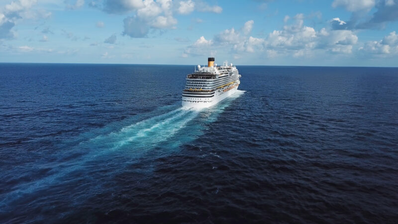 Back of the cruise ship and its beautiful wake on the blue sea surface, seascape. Stock. Aerial view of a beautiful white cruise liner in a sunny day on blue cloudy sky background. 