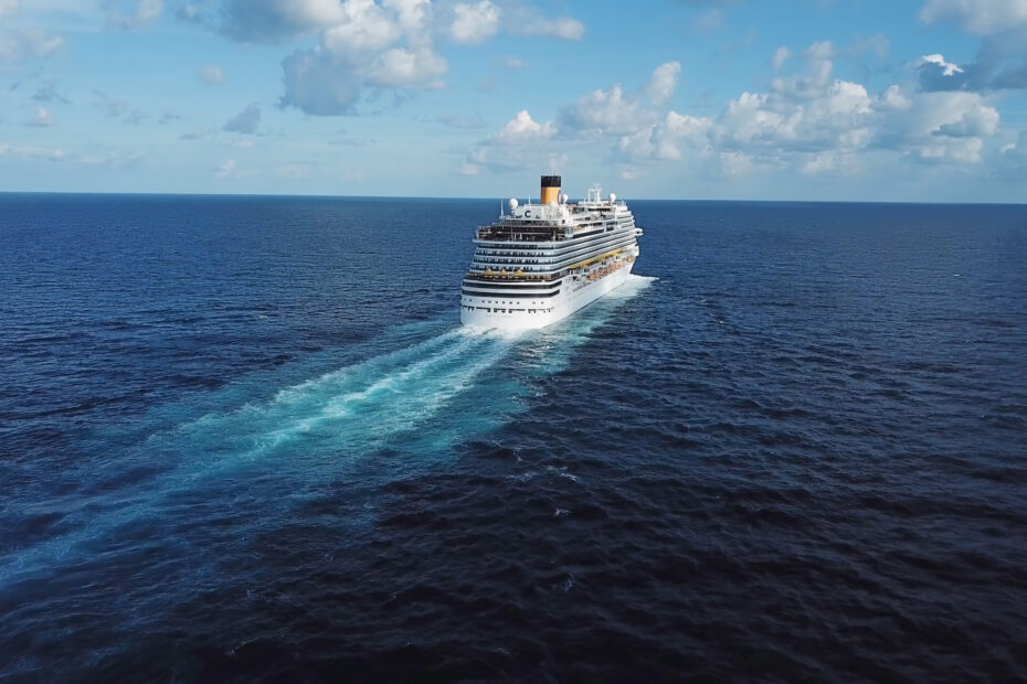 Back of the cruise ship and its beautiful wake on the blue sea surface, seascape. Stock. Aerial view of a beautiful white cruise liner in a sunny day on blue cloudy sky background.