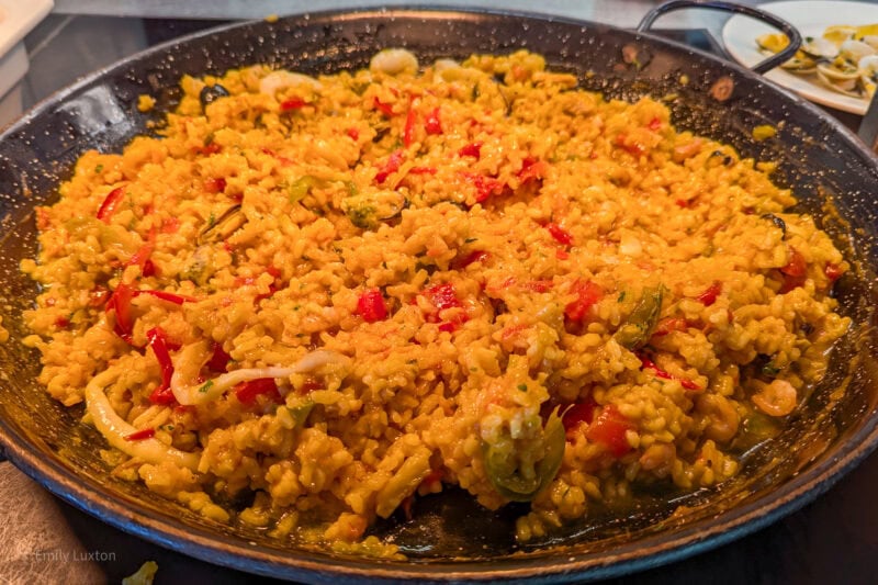 close up of a large black pan full of paella rice with chopped red and green peppers.