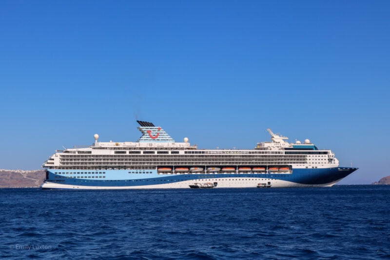 Marella Explorer cruise ship in the ocean with blue sea all around. The ship has a two toned blue base, white exterior and a large cyan funnel with the Tui logo on it - a red smile with a dot above one end.