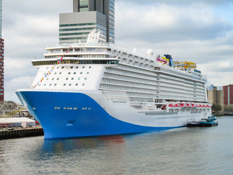 Modern Norwegian cruiseship or cruise ship liner in port of Rotterdam with city skyline during sunrise twilight and picturesque harbor scenery with other boats and skyscrapers