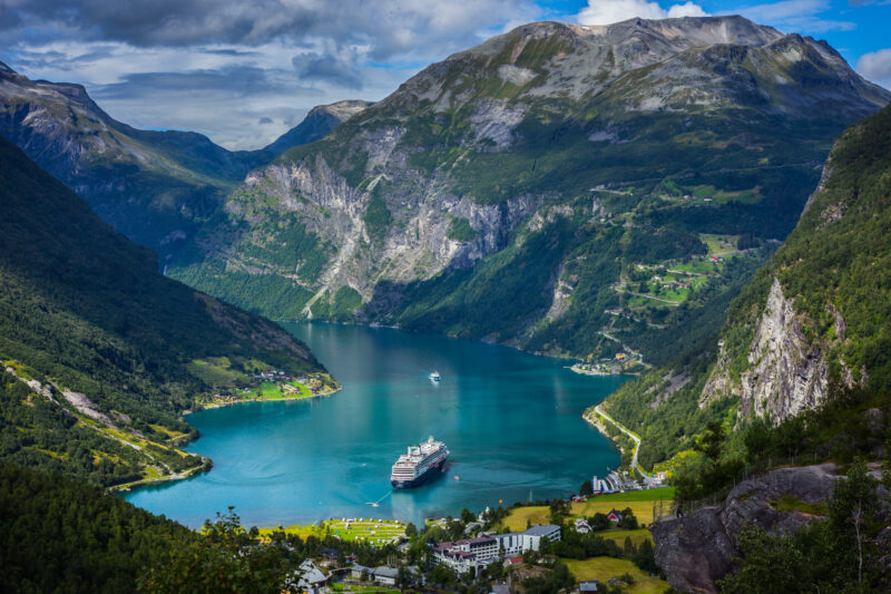 aerial view of a fjord with bright blue water surroudned by snowcapped mountains in norway with a white cruise ship in the middle of the fjord