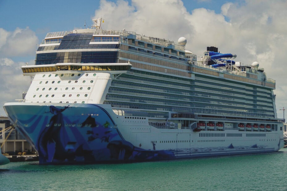 large white cruise ship with a blue front in a port in the caribbean with cyan water in front