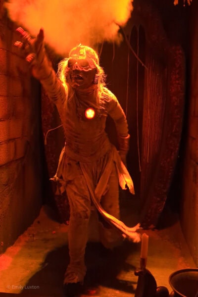 actor in a mummy costume reaching up with one clawed hand surrounded by dry ice and lit by orange light. In a haunted house at Universal Orlando Halloween Horror Nights