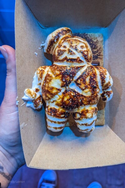 hand holding a brown card tray with a toasted marshmallow shaped like a man