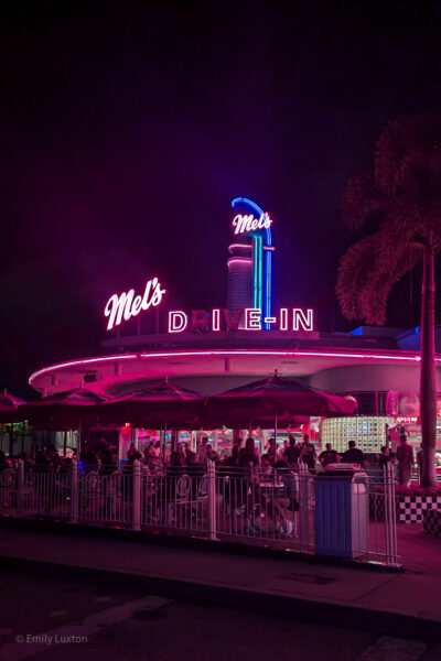 Diner at night lit in pink neon, there is a palm tree next to the diner and a large crowd of people seated outside. A pink neon sign on the roof reads Mel's Drive-in but the R and V are not lit so it looks like Mel's Die-In.

How Scary are Universal Orlando Halloween Horror Nights?