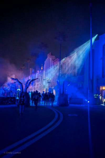 Street in Universal Studios Orlando at night with green and pink lights catching on a fog of dry ice and several people siloutted against the light.