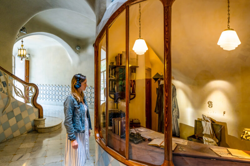 mulher usando um vestido branco, jaqueta jeans azul e fones de ouvido olhando para uma vitrine com uma mesa e várias peças de roupa