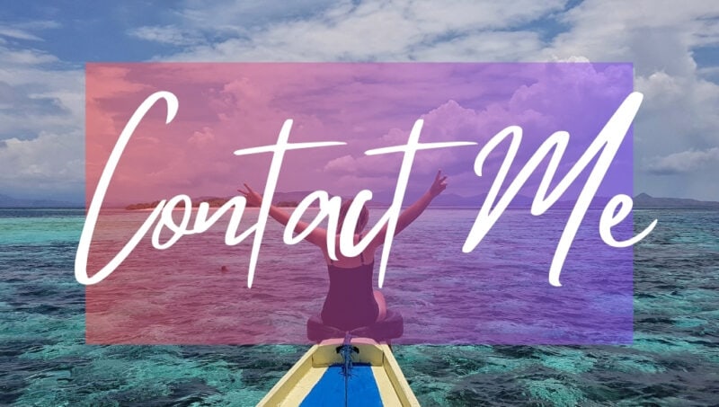 Contact Me written in white text over an opaque pink box on top of a photo. The photo shows the figure of a woman on the prow of a wooden boat painted yellow and blue surrounded by clear turquoise sea. The woman has her arms in the air. 