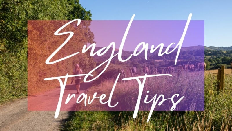 England Travel Tips written in white text over an opaque pink box on top of a photo of a path in the English countryside. There are trees on the left side and a grassy field with horses on the right. A woman is walking along the path in the distance wearing shorts and a white t-shirt.