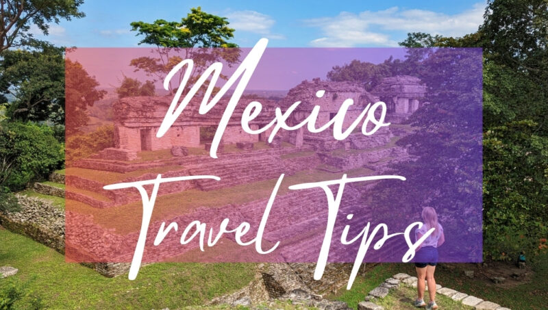 Mexico Travel Tips written in white text over an opaque pink box on top of a photo of some grey stone Mayan ruins on a grassy hill. In the foreground is travel blogger Emily Luxton, standing on the edge of a grassy hill looking out towards the ruins. She is wearing dark blue denim shorts and a white t-shirt and has her hands in her pockets.