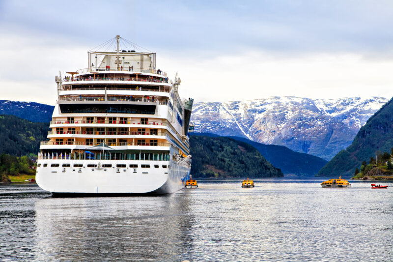 white cruise ship docked in the sea with snowcapped mountains behind on an overcast day 