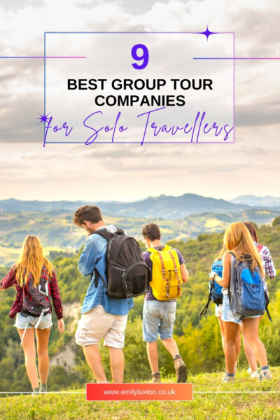 9 best group tour companies for solo travellers - written in a white box on top of a photo showing a group of youg adults carrying backpacks and hiking in front of a lush green landscape. 