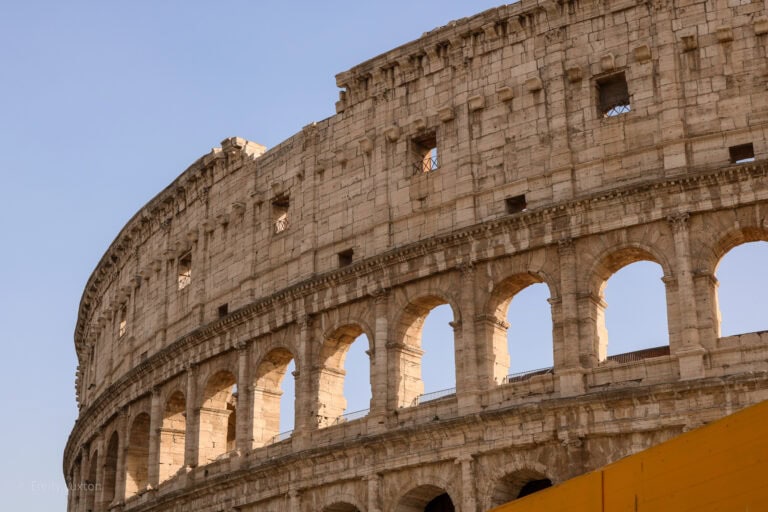 close up of the top section of the Colosseum in Rome, a large circular building of beige stone with empty arched windows in a row around it | Is Rome Safe for Solo Female Travellers