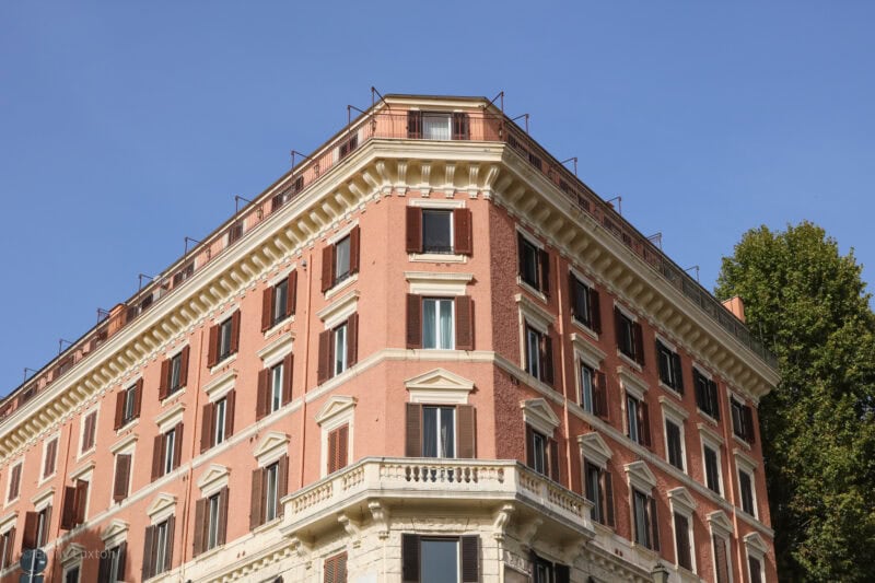 corner of a large pink apartment building with shuttered windows against a cledar blue sky on a sunny morning