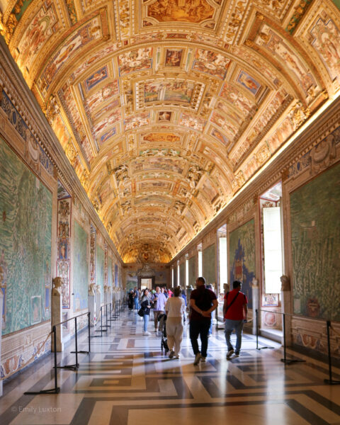 hallway in the Vatican with marble floor, green walls, and a high, arching ceiling covered in gold carvings.