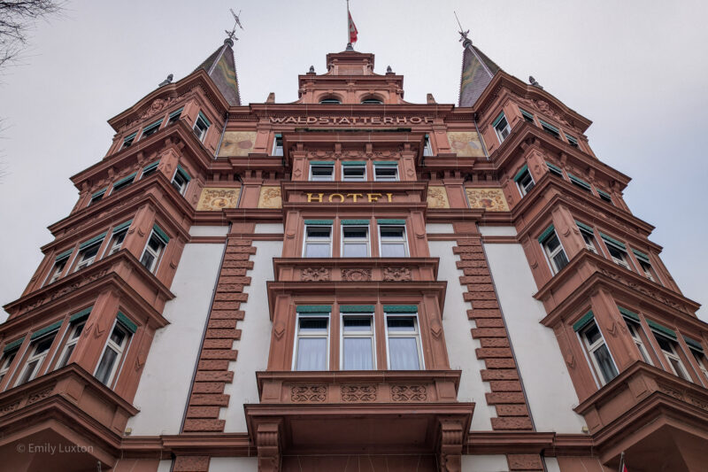 looking up at the front of Hotel Waldstätterhof in Lucerne, a grand building with red bricks and turrets on the roof.