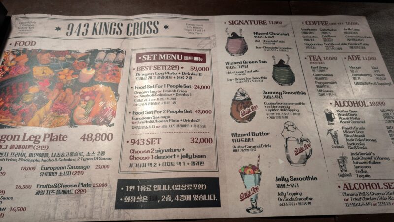 The image shows a menu from a restaurant named "943 Kings Cross." The menu is designed to look like a newspaper and includes various sections for food, set menus, signature drinks, coffee, tea, ade, and alcohol. The menu items are listed with their prices and descriptions, and some items have illustrations.