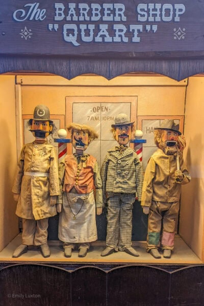 Four mannequins dressed in vintage clothing stand in a display labeled "The Barber Shop 'Quart'."