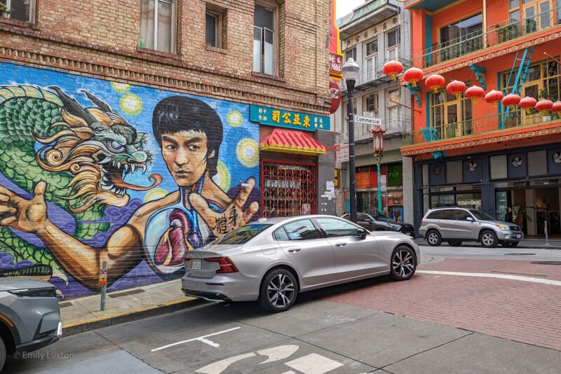 A vibrant mural on a brick building wall in Chinatown, featuring a green dragon and a person in a martial arts pose, with Chinese characters and architectural elements.