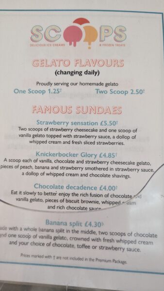 A menu from Scoops, a place offering delicious ice creams and frozen treats. The menu lists gelato flavors that change daily, with prices for one scoop at £1.25 and two scoops at £2.50. It also features a section for famous sundaes. Each sundae description includes the ingredients and toppings. Prices marked with a † are not included in the Premium Package.