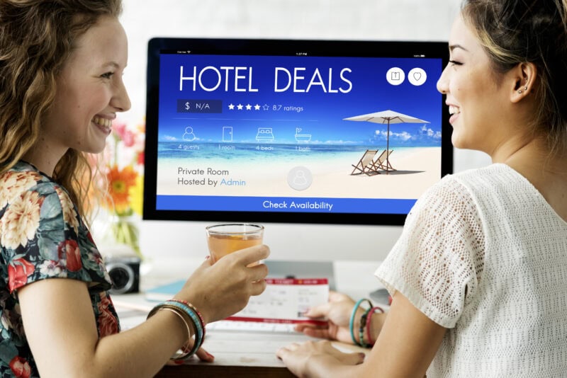 Two people viewing a hotel booking website on a computer screen. The screen is blue and has the words Hotel Deals written on it. 